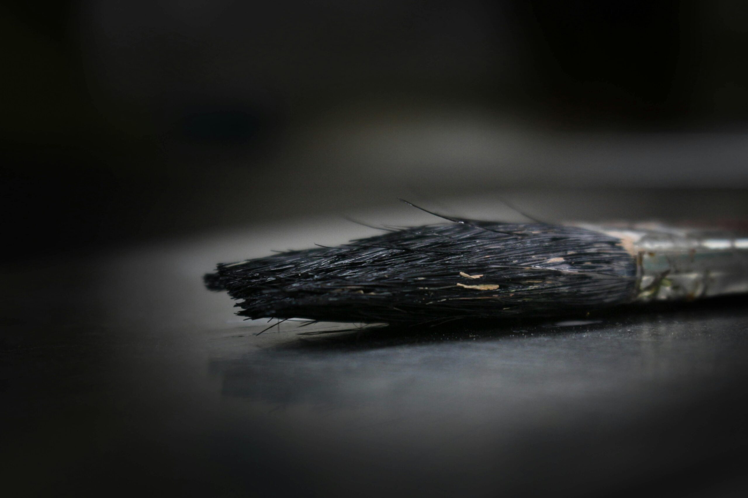 Detailed macro shot of a worn paintbrush lying on a reflective dark surface, showing its rustic texture.